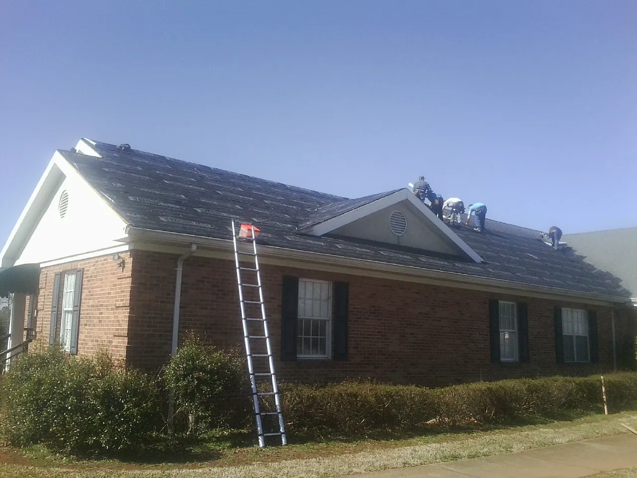 Crew tearing shingles off a brick ranch roof with a ladder set — Metal Roof Repair work by our crew in Quantico