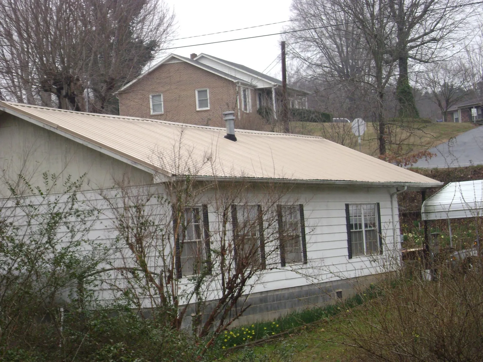 Tan metal roof on a white sided house set into a hillside — Commercial Roofing by Roofing Brothers in Quantico